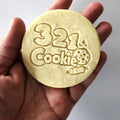 A real baked cookie stamped with the full 321 Cookie logo, held in hand