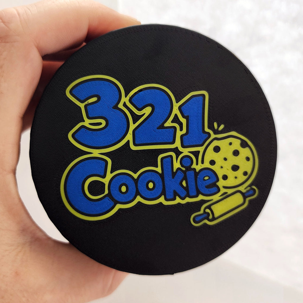 Hand holding the full-color 321 Cookie logo lid, close-up of the blue and yellow logo