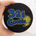 Hand holding the full-color 321 Cookie logo lid, close-up of the blue and yellow logo